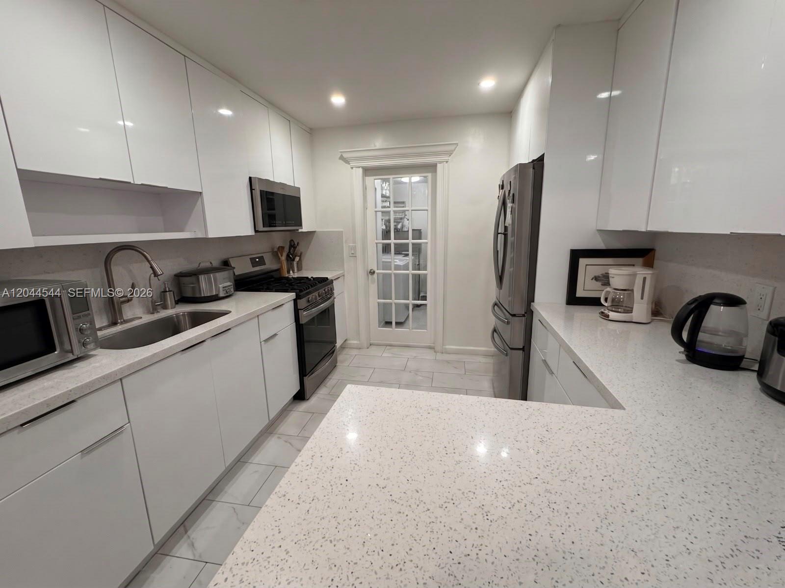 A modern kitchen features white cabinetry, quartz countertops, stainless steel appliances, and a glass-paned door — 974 SE 1st St # 974, Hialeah FL 33010, HIALEAH, FL