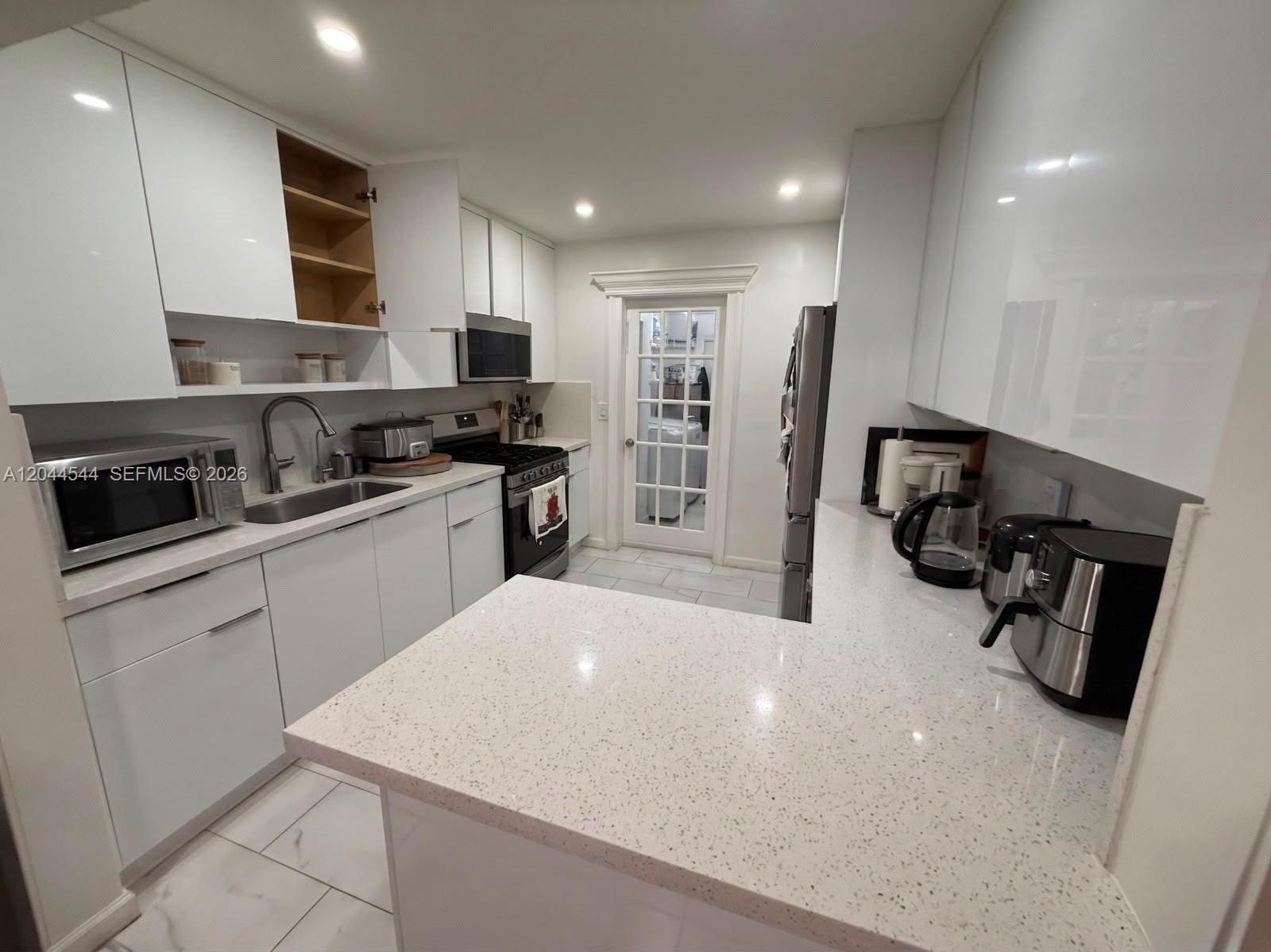 A modern kitchen features white cabinets, quartz countertops, stainless steel appliances, and tile flooring — 974 SE 1st St # 974, Hialeah FL 33010, HIALEAH, FL