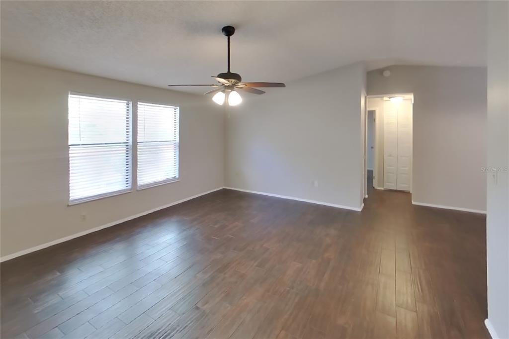 An empty living room features light gray walls, dark wood-look flooring, and a ceiling fan — 8102 CHICKASAW LANE, PORT RICHEY, FL
