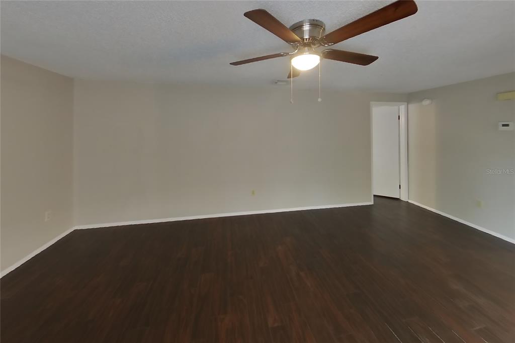 A living room with dark wood-look flooring, light-colored walls, and a ceiling fan — 8102 CHICKASAW LANE, PORT RICHEY, FL