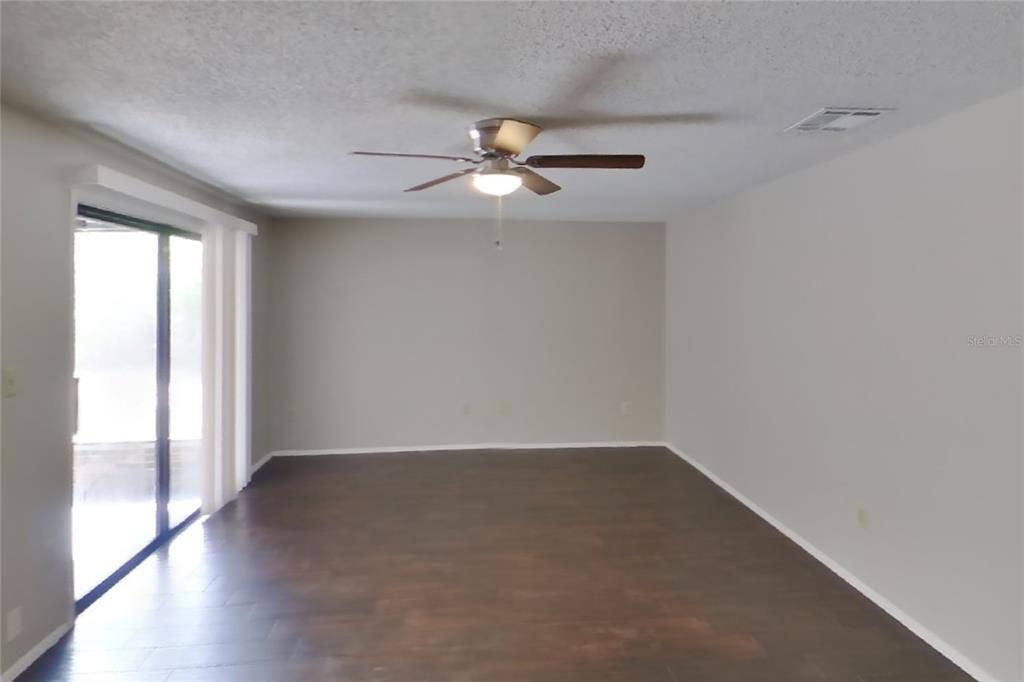 An empty living room features dark wood-look flooring, light gray walls, and a ceiling fan — 8102 CHICKASAW LANE, PORT RICHEY, FL