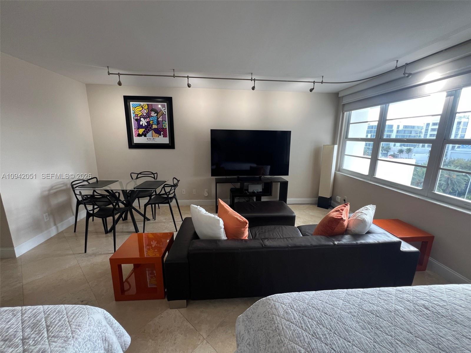 A living and dining area features a dark leather sofa, glass table, and large windows — 100 Lincoln Rd # 716, Miami Beach FL 33139, MIAMI BEACH, FL