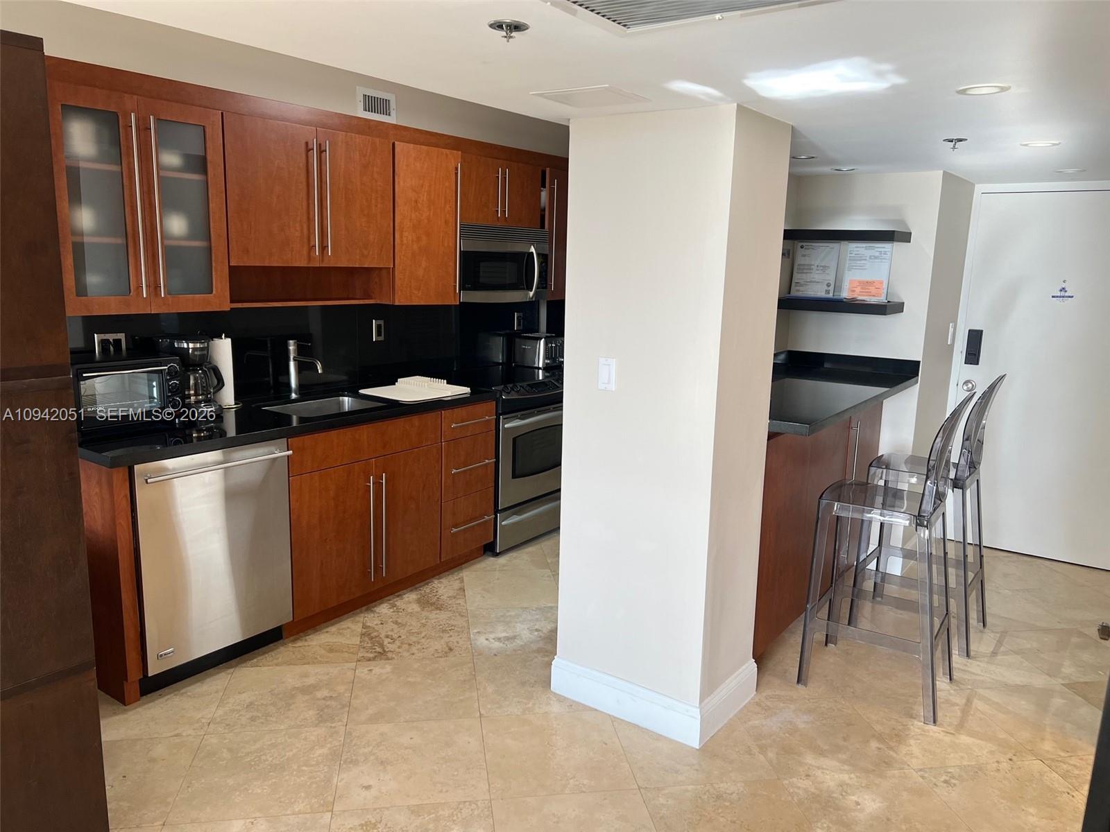 A kitchen features wood cabinets, black countertops, stainless steel appliances, and a breakfast bar — 100 Lincoln Rd # 716, Miami Beach FL 33139, MIAMI BEACH, FL