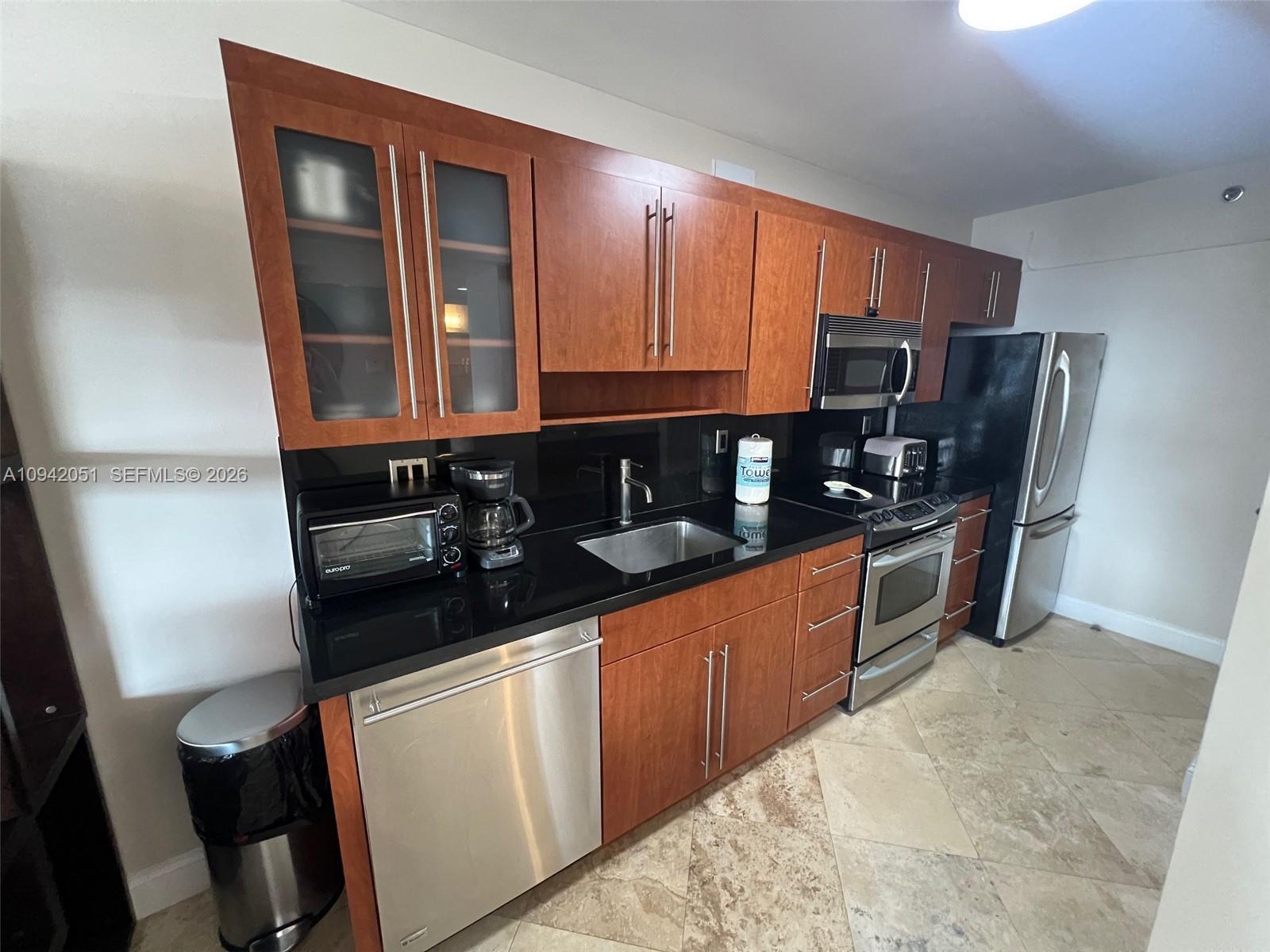 A kitchen features cherry wood cabinets, black countertops, stainless steel appliances, and tiled flooring — 100 Lincoln Rd # 716, Miami Beach FL 33139, MIAMI BEACH, FL