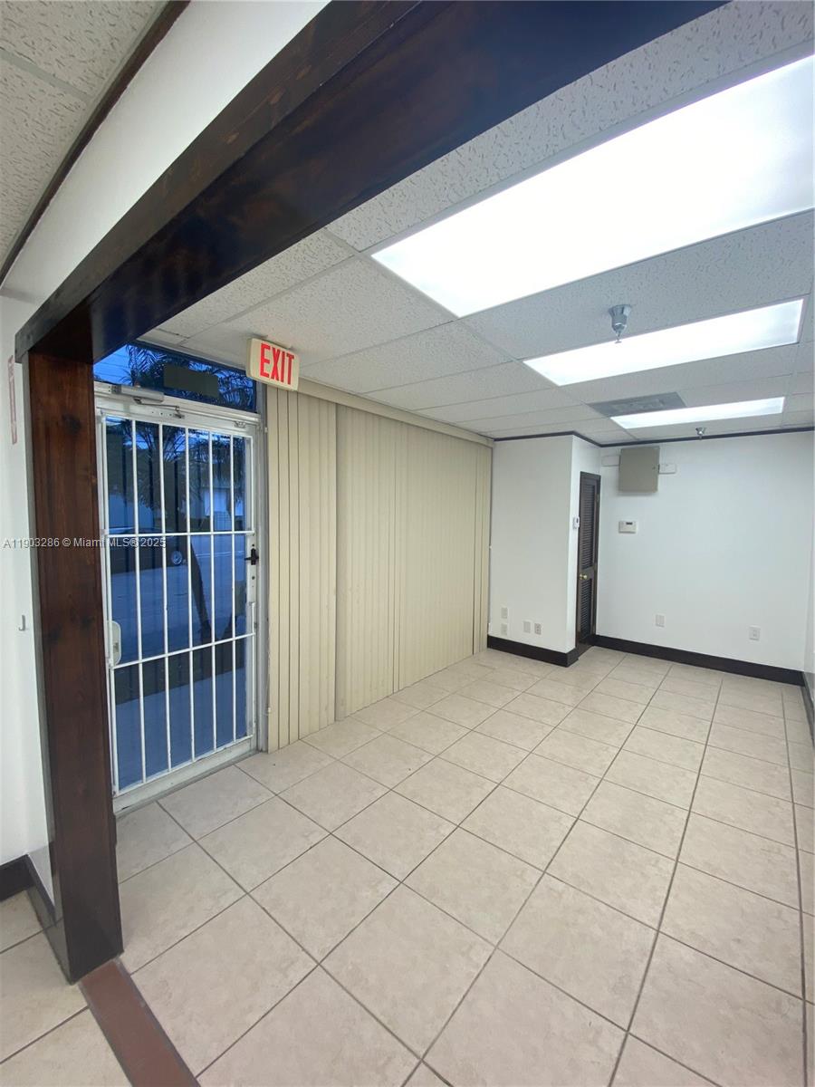 An empty office space features tiled floors, a drop ceiling, and a security-gated glass door — 8202 NW 70th St # 6994, Medley FL 33195, MEDLEY, FL