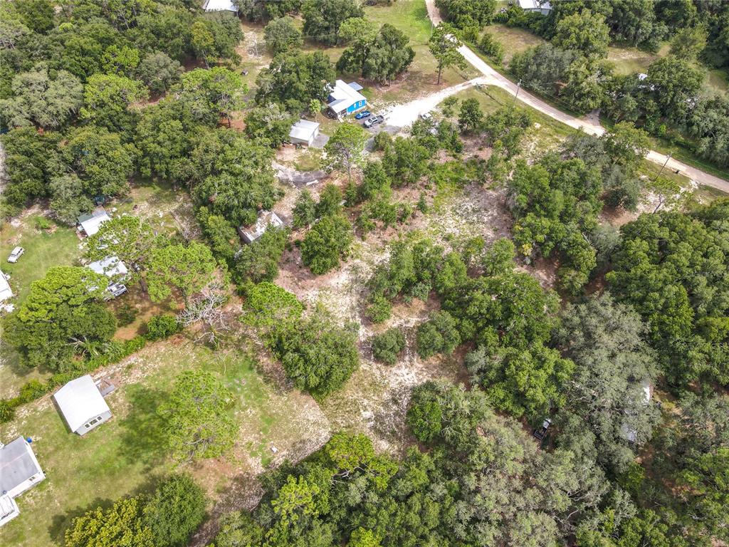 An aerial view shows a wooded lot with several small buildings and a dirt driveway — 114 PLANTATION WAY, HAWTHORNE, FL