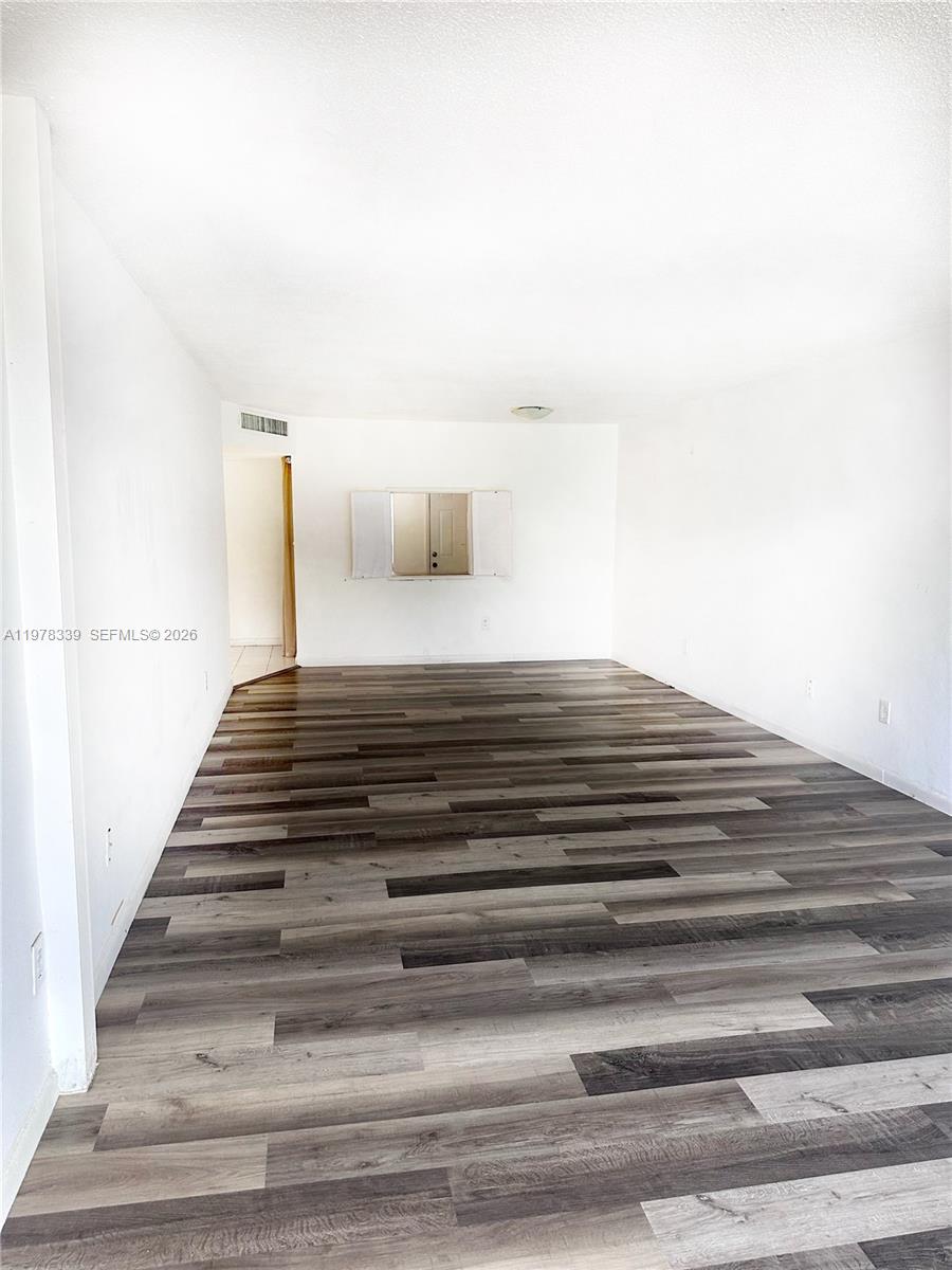 An empty room features white walls and gray wood-look plank flooring — 1501 NE 191st St # C312, Miami FL 33179, MIAMI, FL