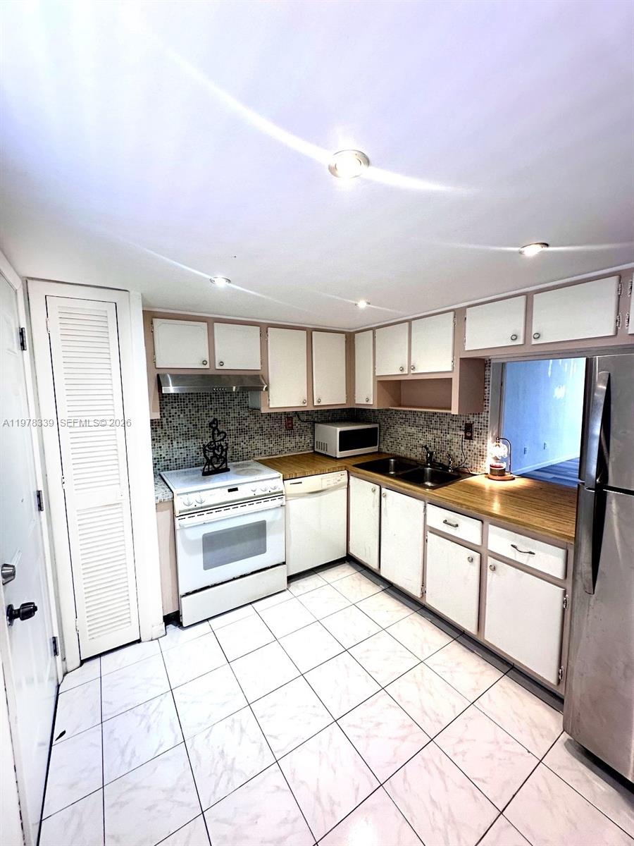 A kitchen features white cabinets, a white stove, a dishwasher, and light-colored tile flooring — 1501 NE 191st St # C312, Miami FL 33179, MIAMI, FL