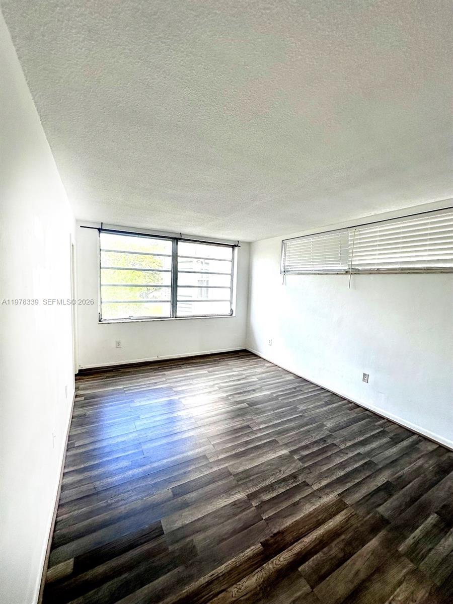 An empty room features dark wood-look flooring, white walls, and windows with horizontal blinds — 1501 NE 191st St # C312, Miami FL 33179, MIAMI, FL
