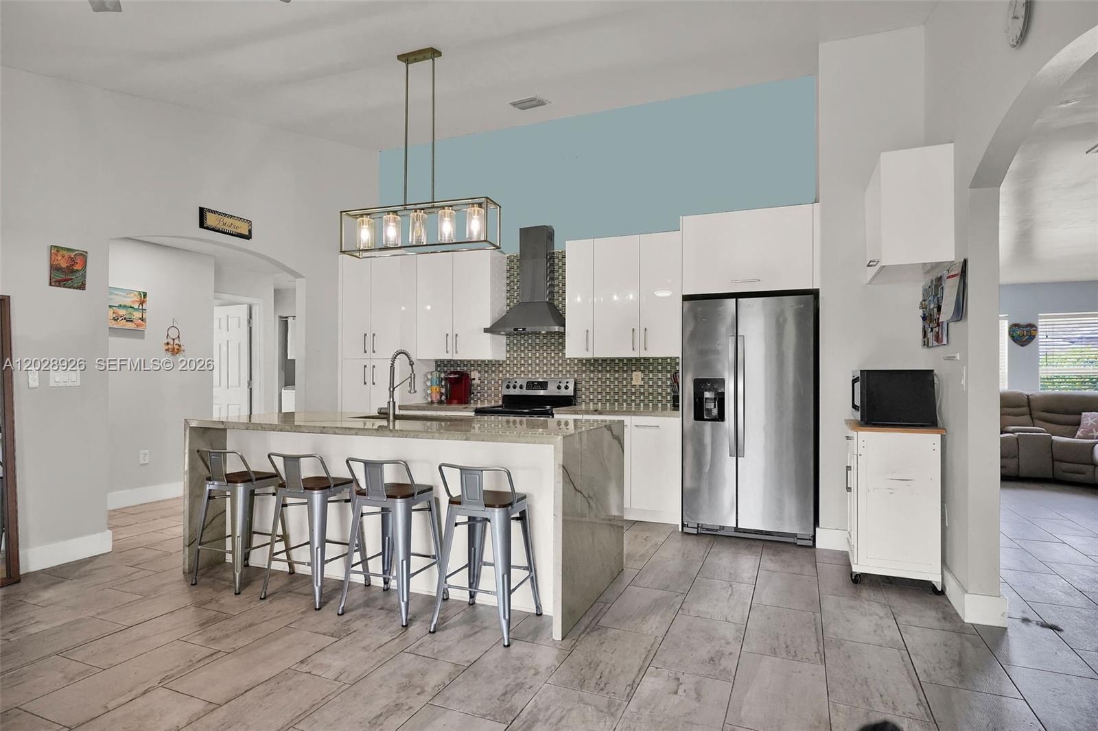 A kitchen features white cabinets, a stone-topped island with four stools, and stainless steel appliances — 14244 SW 163rd Ter, Miami FL 33177, MIAMI, FL