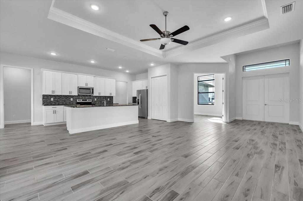 A modern open-concept kitchen and living area with white cabinetry, gray tile flooring, and recessed lighting — 459 NE 2ND PLACE, CAPE CORAL, FL