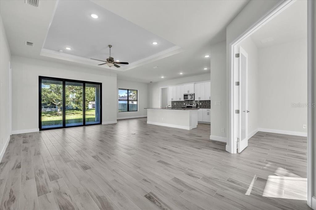 An open-concept living area features light wood-look tile floors, a tray ceiling, and a kitchen — 459 NE 2ND PLACE, CAPE CORAL, FL