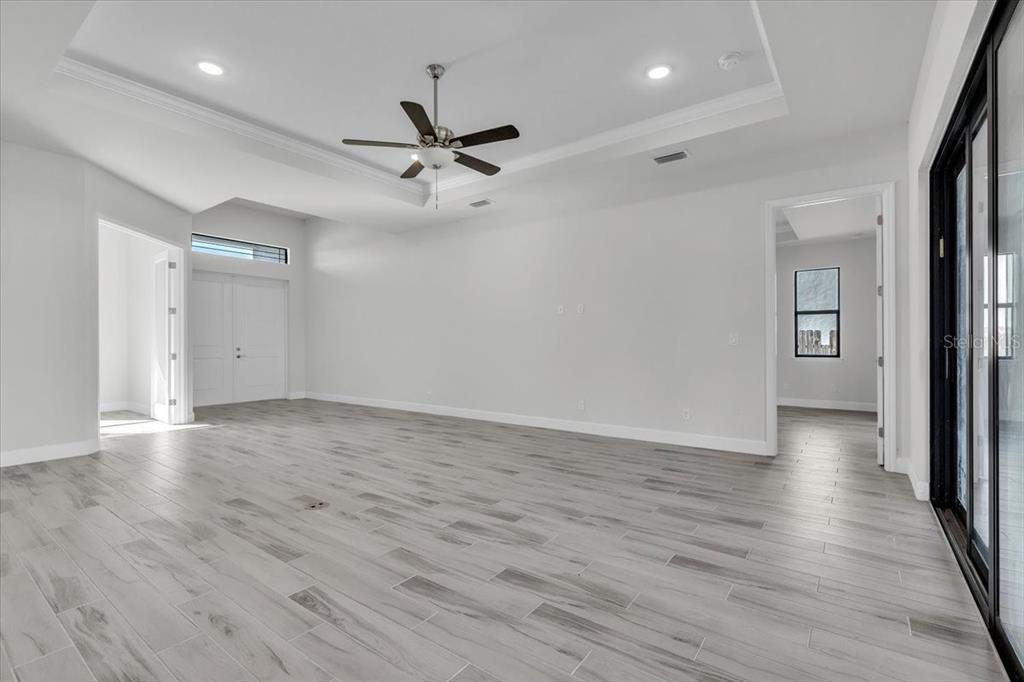 A spacious, empty room features light gray wood-look tile flooring, a tray ceiling, and recessed lighting — 459 NE 2ND PLACE, CAPE CORAL, FL