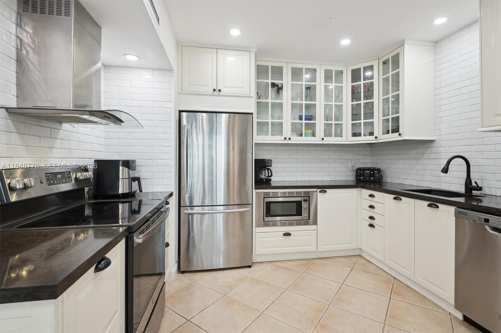 A kitchen features white cabinets, stainless steel appliances, black countertops, and white subway tile backsplash — 3505 S OCEAN DR # 1015, Hollywood FL 33019, HOLLYWOOD, FL