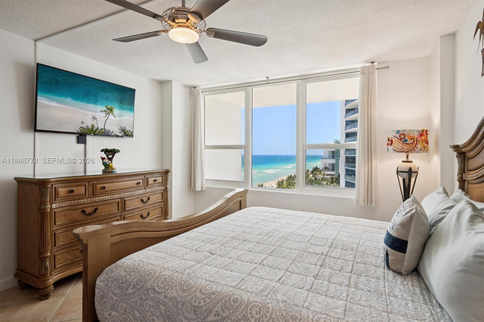 A bedroom with a wooden bed frame, dresser, ceiling fan, and a view of the ocean — 3505 S OCEAN DR # 1015, Hollywood FL 33019, HOLLYWOOD, FL