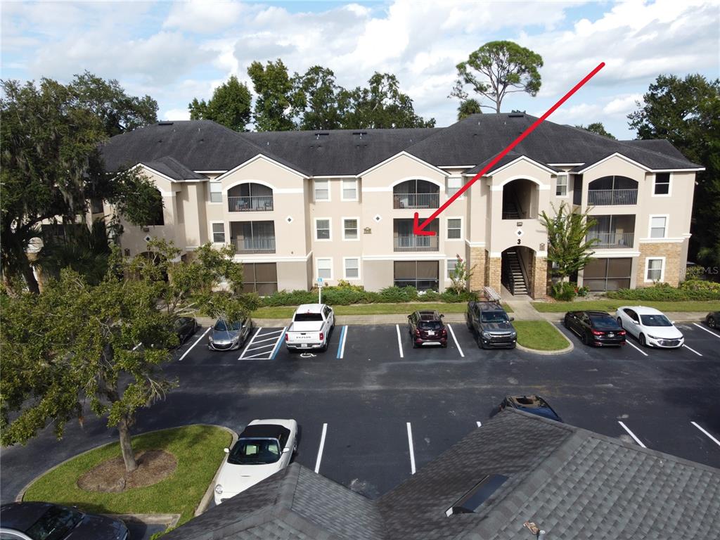An exterior view of a multi-story apartment building with a red arrow pointing to a balcony — 940 VILLAGE TRAIL UNIT 3-205, PORT ORANGE, FL