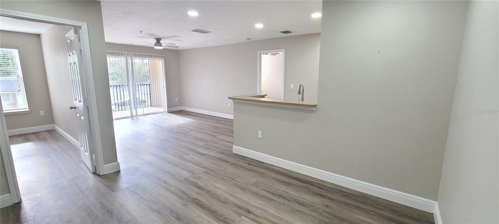 An interior view shows a living area with wood-look flooring and a kitchen pass-through window — 940 VILLAGE TRAIL UNIT 3-205, PORT ORANGE, FL