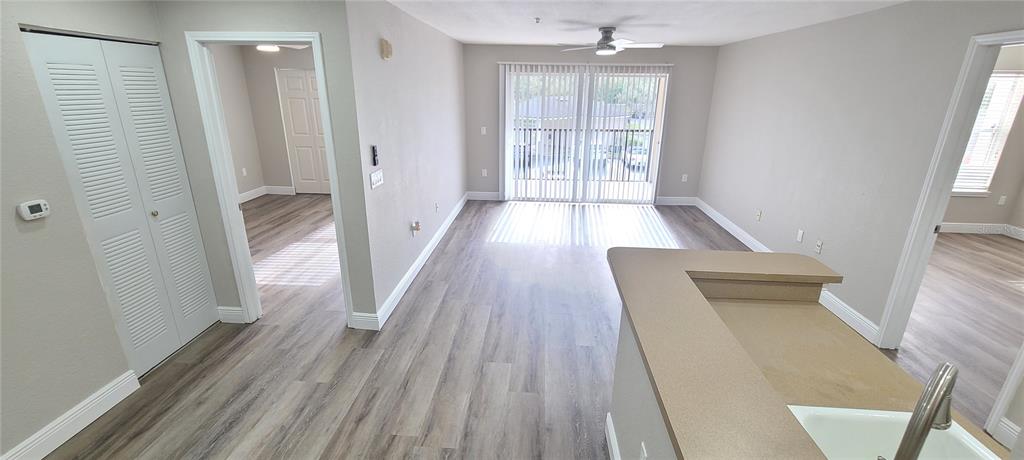 A living room with light wood-look flooring, a ceiling fan, and sliding glass balcony doors — 940 VILLAGE TRAIL UNIT 3-205, PORT ORANGE, FL