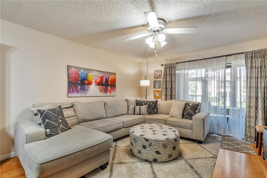 A living room features a light gray sectional sofa, a patterned ottoman, and a ceiling fan — 2400 WINDING CREEK BOULEVARD UNIT 24-102, CLEARWATER, FL