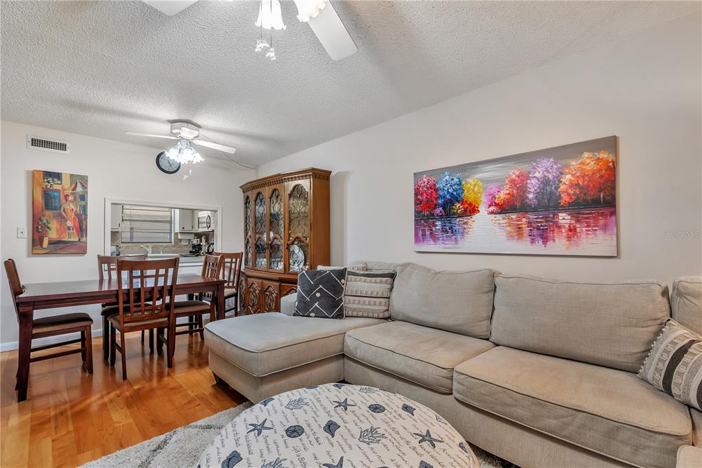 A living room with a sectional sofa, dining table, and a large landscape wall painting — 2400 WINDING CREEK BOULEVARD UNIT 24-102, CLEARWATER, FL