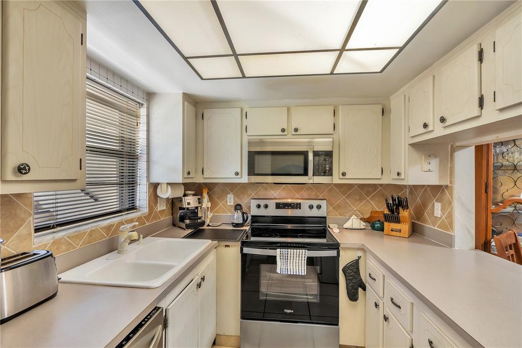 A kitchen with white cabinets, a double sink, stainless steel appliances, and a tiled backsplash — 2400 WINDING CREEK BOULEVARD UNIT 24-102, CLEARWATER, FL