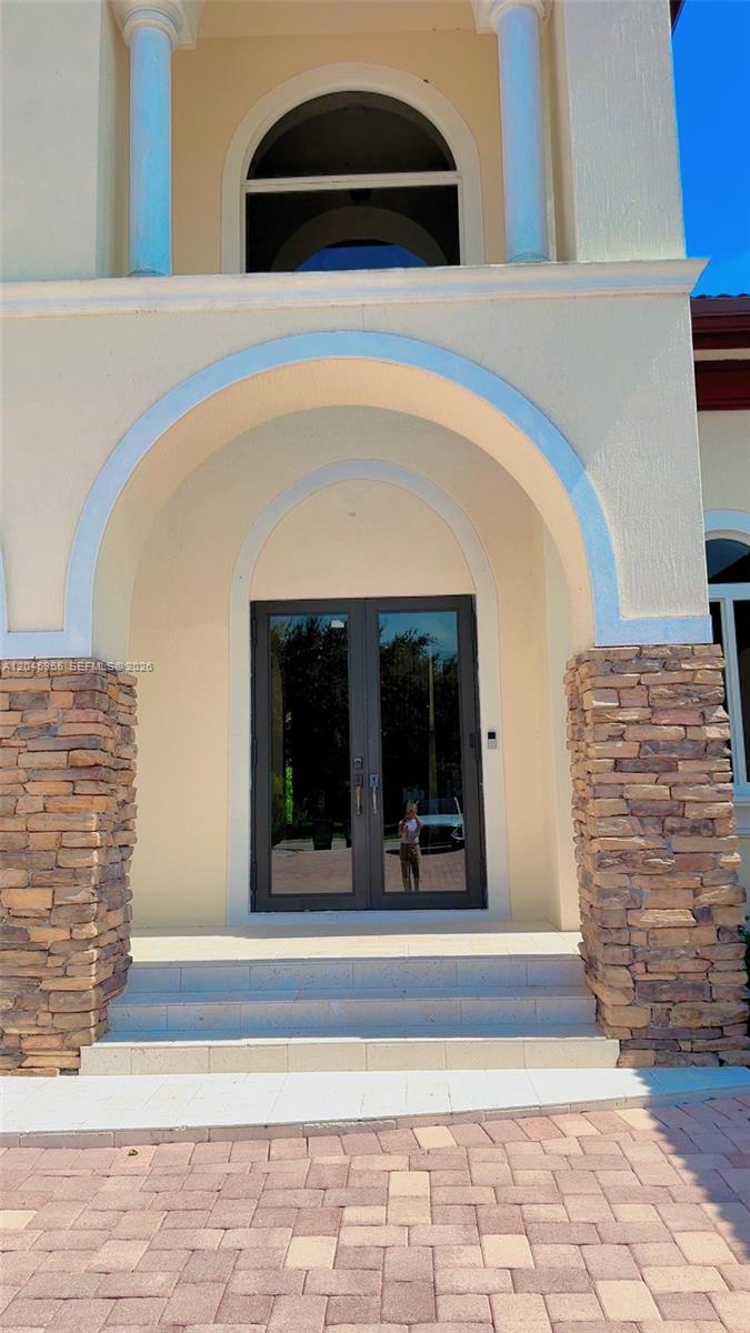 The exterior of a house features a stone-accented arched entryway with double glass doors — 12802 Grand Oaks Dr # 0, Davie FL 33330, DAVIE, FL