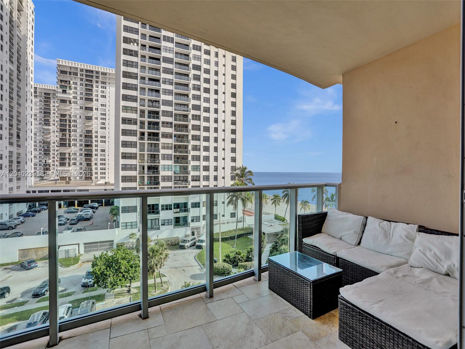 A balcony with wicker furniture overlooks a parking lot, nearby high-rise buildings, and the ocean — 2501 S Ocean Dr, Hollywood FL 33019, HOLLYWOOD, FL