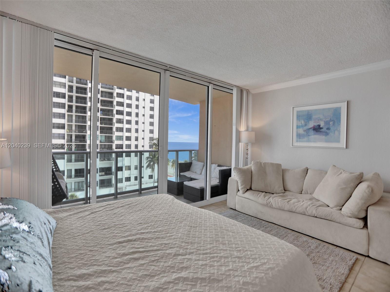 A bedroom features a bed, a sofa, and a balcony overlooking the ocean and buildings — 2501 S Ocean Dr, Hollywood FL 33019, HOLLYWOOD, FL