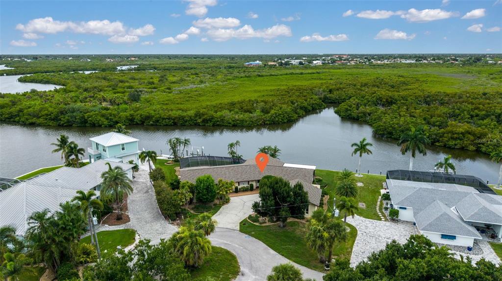 An aerial view shows a waterfront house with a pool cage and surrounding tropical vegetation — 4589 COLLEEN STREET, PORT CHARLOTTE, FL