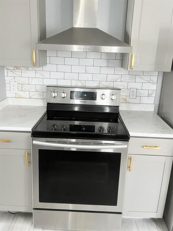A stainless steel stove and range hood are centered between gray cabinets and marble-look backsplash — 2115 SHADY POINT LANE, BRANDON, FL