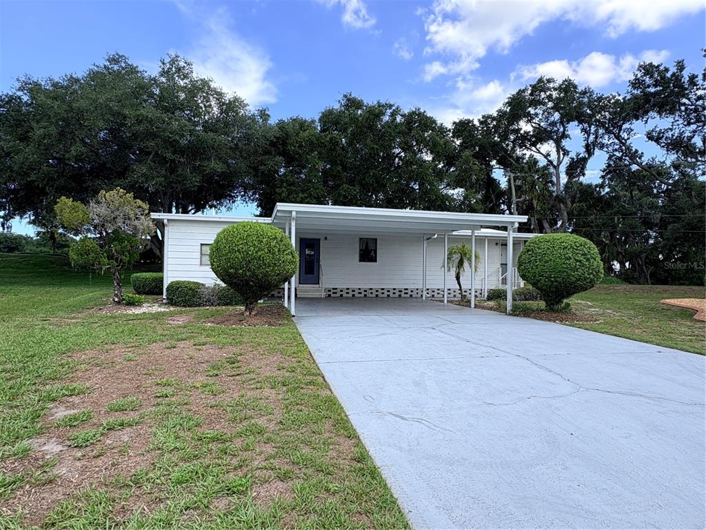 A white single-story house features a large carport, a concrete driveway, and manicured spherical shrubs — 8519 BUCKINGHAM PLACE, PALMETTO, FL