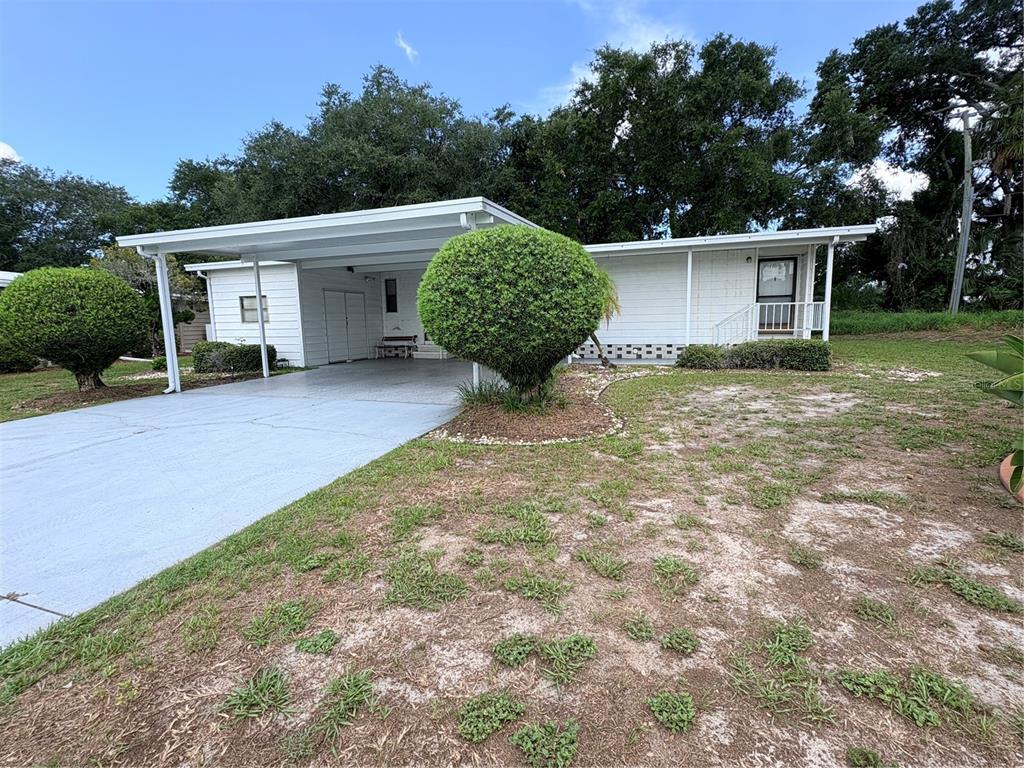 A white single-story house features a carport, a paved driveway, and a manicured front lawn — 8519 BUCKINGHAM PLACE, PALMETTO, FL