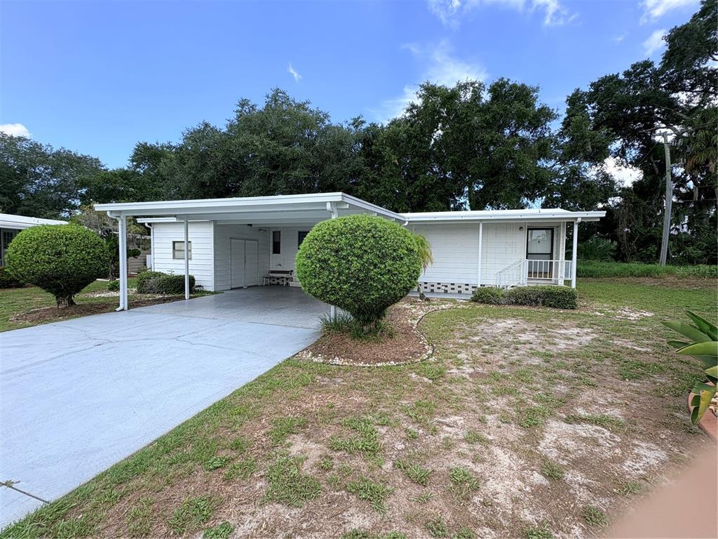 A white single-story house features a carport, a concrete driveway, and two manicured round bushes — 8519 BUCKINGHAM PLACE, PALMETTO, FL
