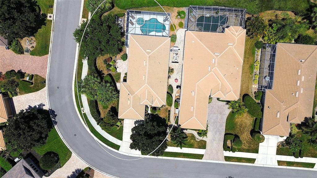 An aerial view shows three suburban houses with tiled roofs, swimming pools, and driveways — 9735 53RD DR E, BRADENTON, FL