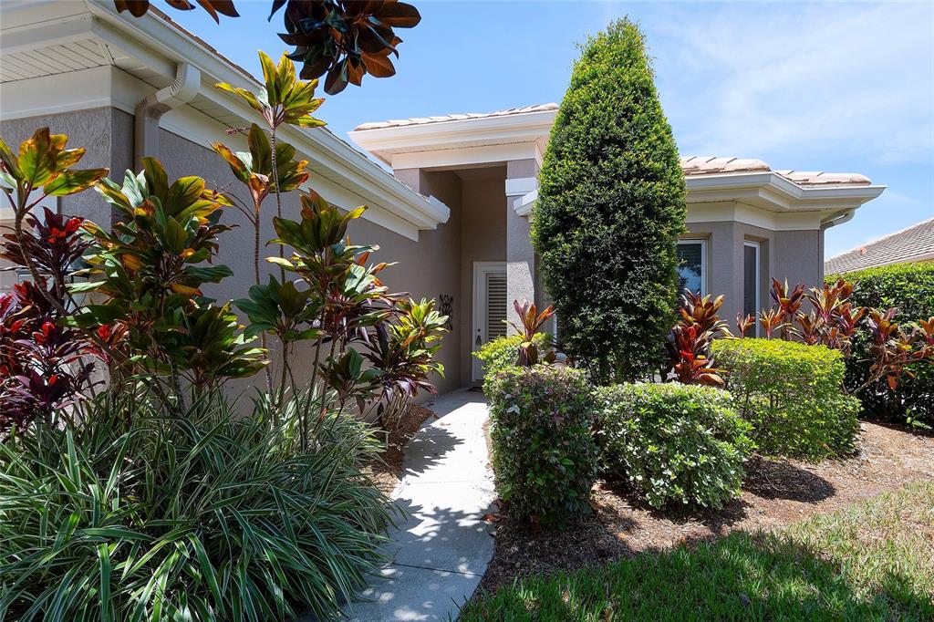 A concrete walkway leads to the front entrance of a house surrounded by lush landscaping — 9735 53RD DR E, BRADENTON, FL
