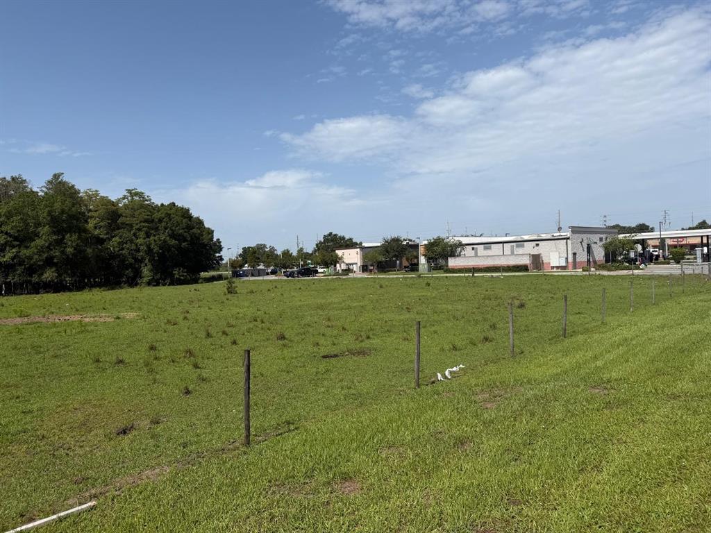 A grassy, fenced-in vacant lot sits in front of a commercial building and trees — 576 TRADEPORT DRIVE, ORLANDO, FL