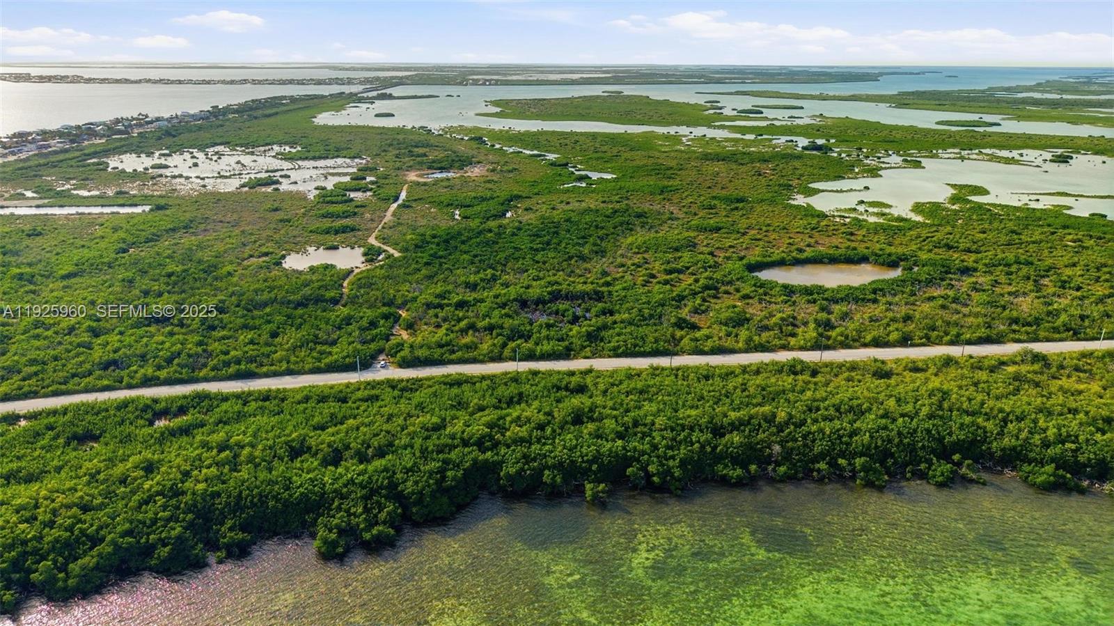 An aerial view shows a road cutting through dense green vegetation and coastal wetlands — 0 Niles Rd, Key Colony FL 33042, KEY COLONY, FL