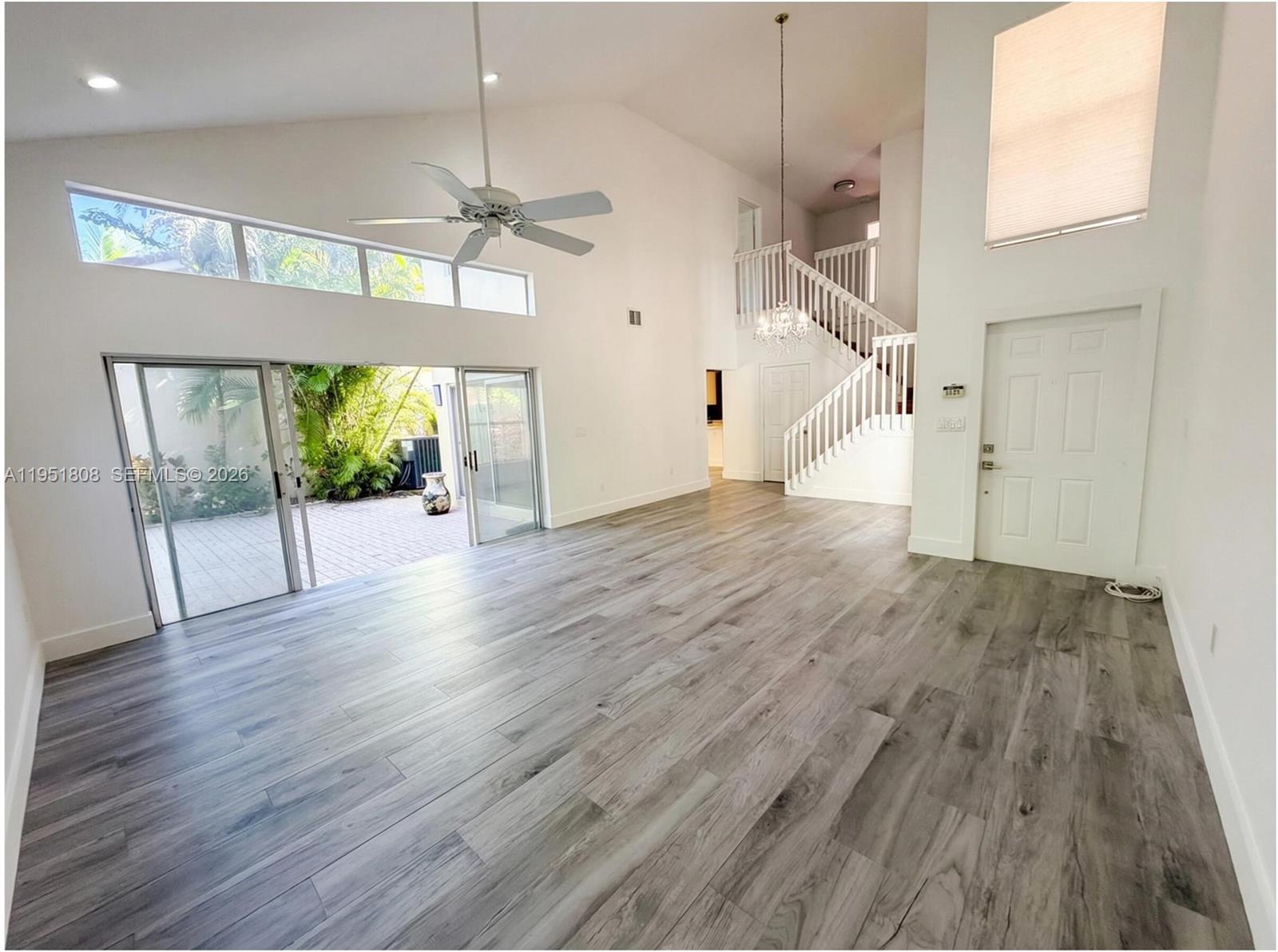 A bright living room features vaulted ceilings, gray wood-look flooring, a staircase, and sliding glass doors — 1145 W Lake St, Hollywood FL 33019, HOLLYWOOD, FL