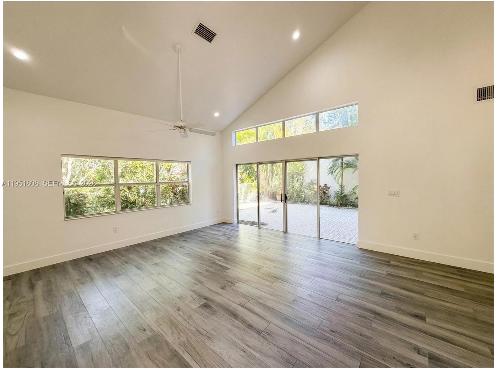 A bright living room features vaulted ceilings, gray wood-look flooring, and large sliding glass doors — 1145 W Lake St, Hollywood FL 33019, HOLLYWOOD, FL