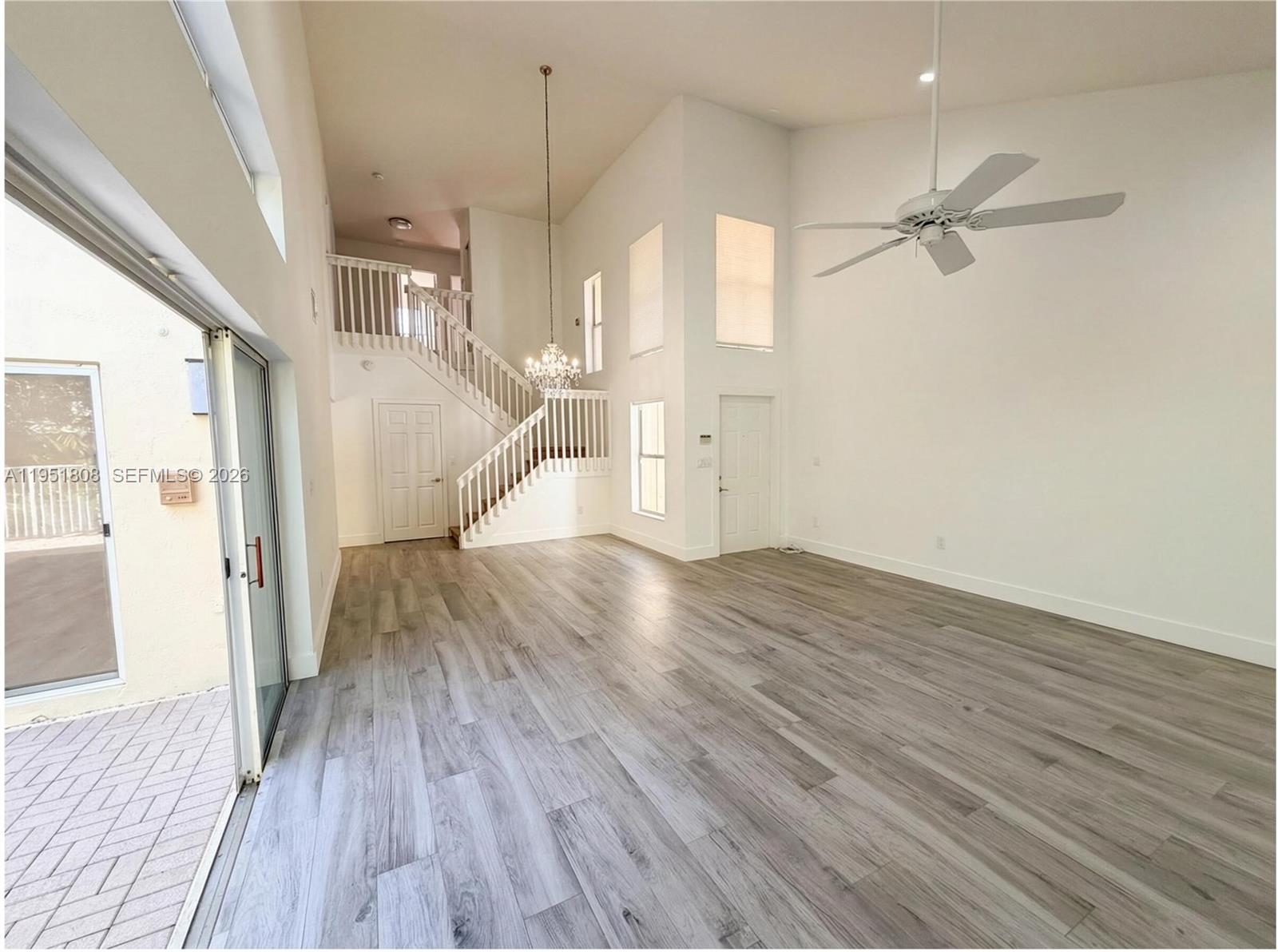 A bright, empty living room with high ceilings, wood-look flooring, a staircase, and sliding doors — 1145 W Lake St, Hollywood FL 33019, HOLLYWOOD, FL