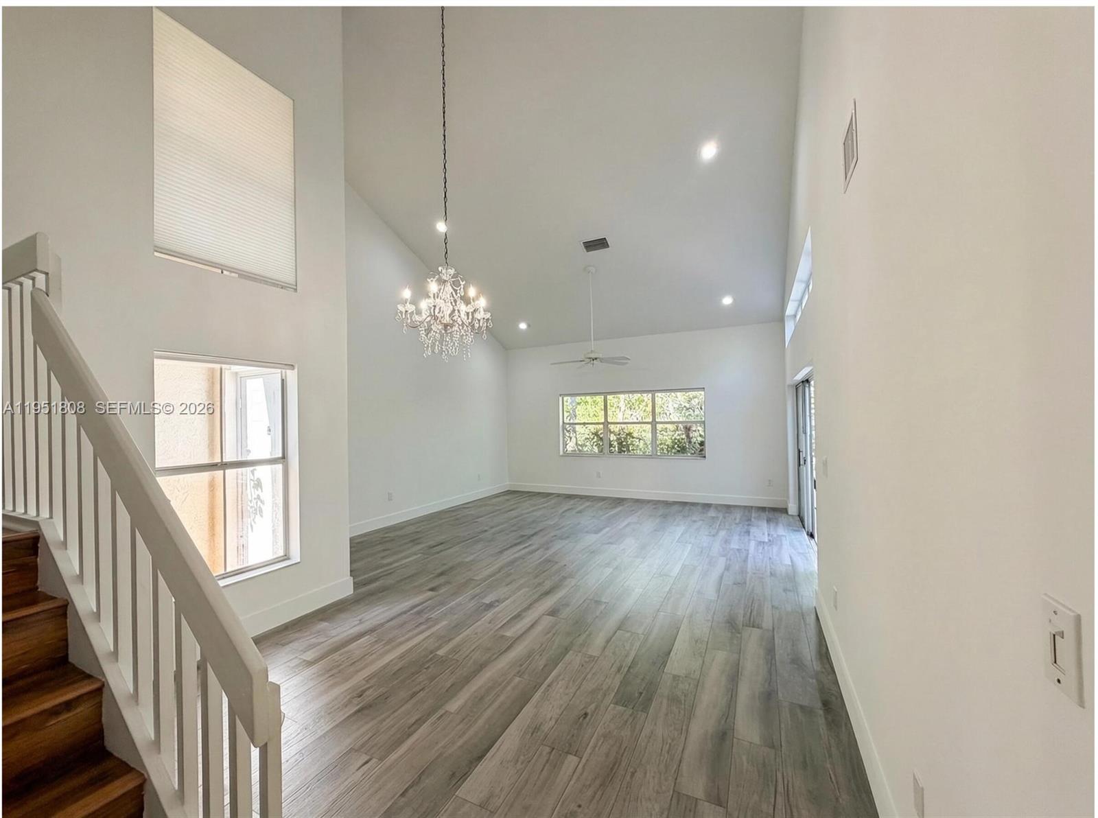 A bright, empty living room features high vaulted ceilings, wood-look flooring, and a crystal chandelier — 1145 W Lake St, Hollywood FL 33019, HOLLYWOOD, FL