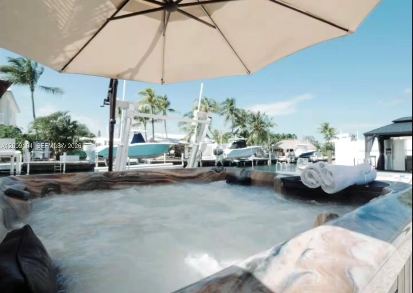 A hot tub sits on a patio overlooking a canal with docked boats and palm trees — 2133 Yellowtail Dr, Marathon FL 33050, MARATHON, FL