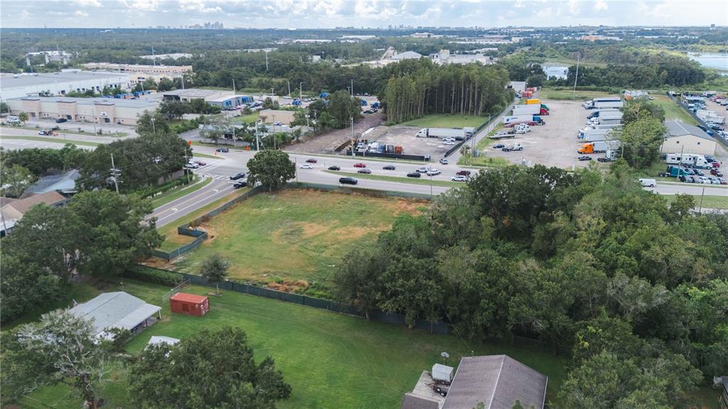An aerial view shows a vacant grassy lot bordered by trees, a road, and nearby buildings — 5406 W LINEBAUGH AVENUE, TAMPA, FL