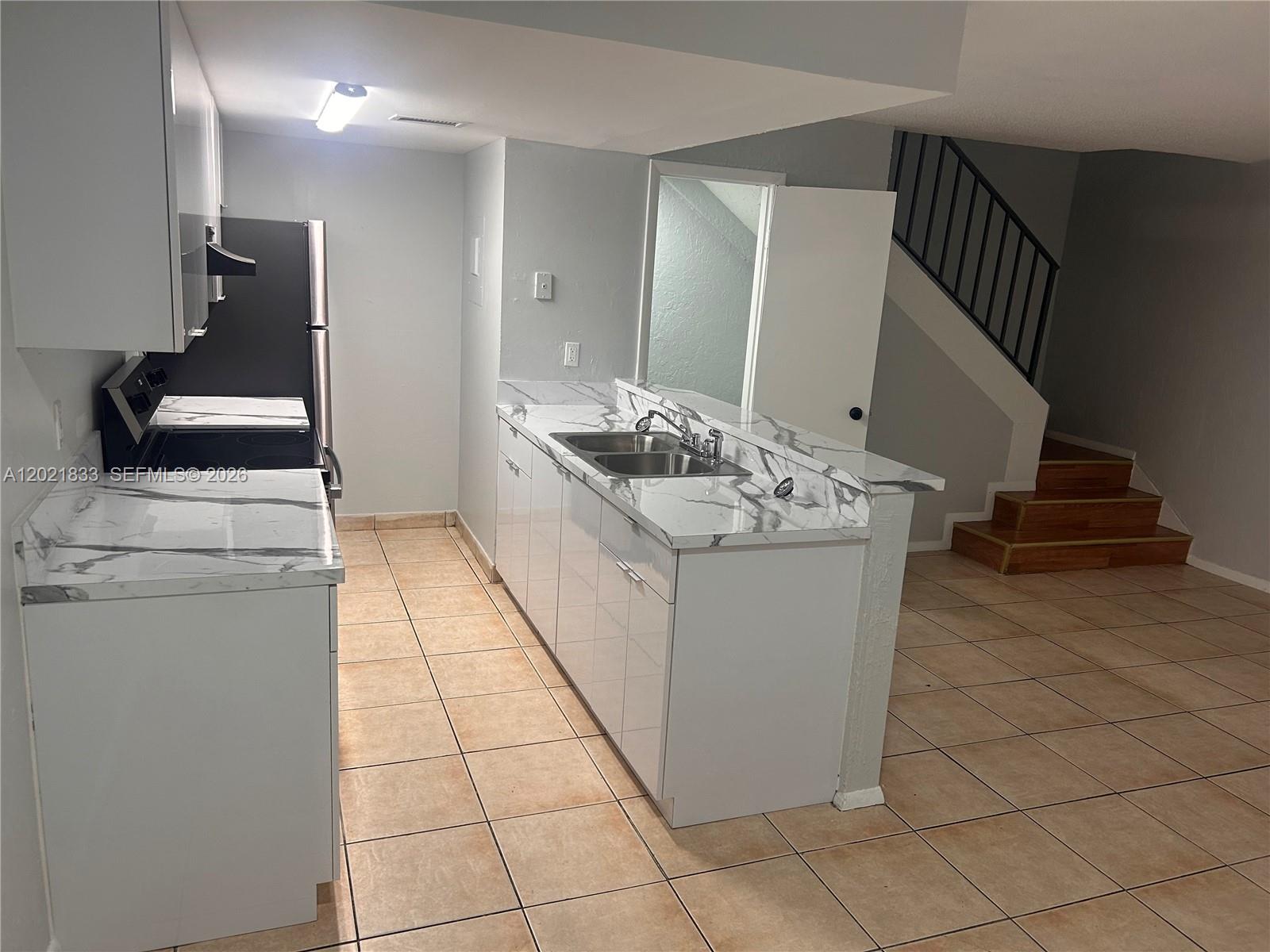 A kitchen features white cabinets, marble-patterned countertops, a stainless steel sink, and tile flooring — 2067 Ilene Ct # 2, Delray Beach FL 33445, DELRAY BEACH, FL