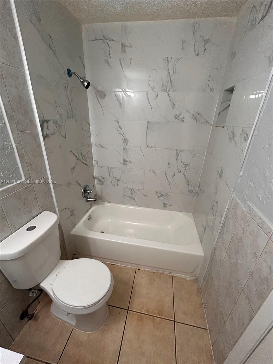 A bathroom features a white toilet, a bathtub, and walls tiled with white marble patterns — 2067 Ilene Ct # 2, Delray Beach FL 33445, DELRAY BEACH, FL