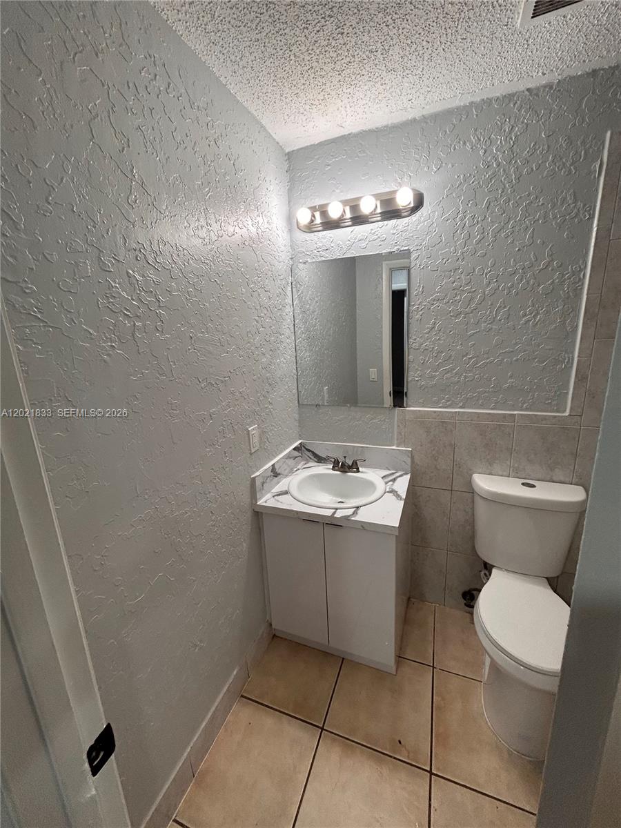 A small bathroom features a white vanity, a mirror, and a toilet on tiled floors — 2067 Ilene Ct # 2, Delray Beach FL 33445, DELRAY BEACH, FL