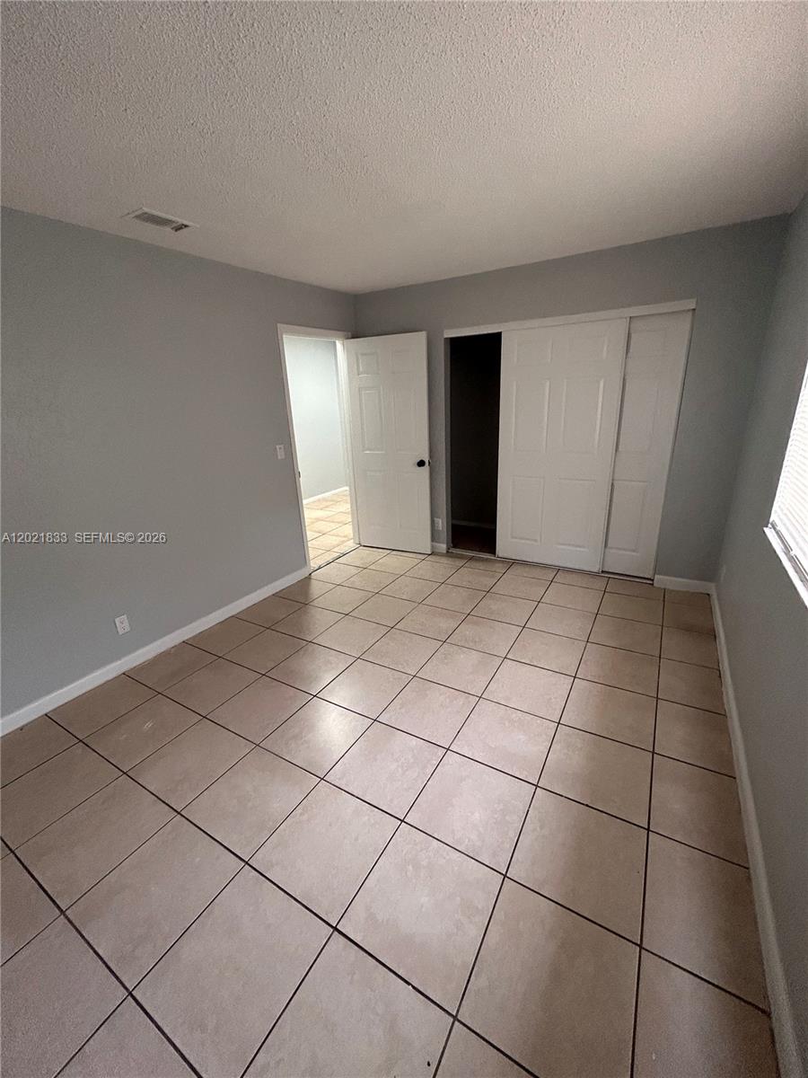 A bedroom features light gray walls, beige tile flooring, a white door, and a closet — 2067 Ilene Ct # 2, Delray Beach FL 33445, DELRAY BEACH, FL