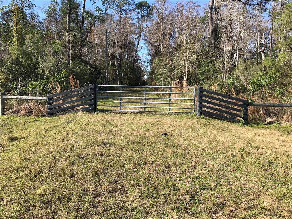 A metal gate sits between two sections of black wooden fencing in a grassy field — PARCEL 2 N FORT CHRISTMAS ROAD, CHRISTMAS, FL