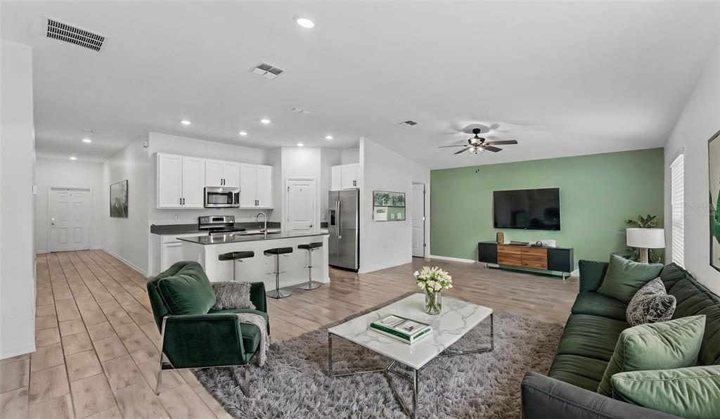 An open-concept living room and kitchen featuring white cabinets, a green accent wall, and furniture — 272 PERSHING STREET, BARTOW, FL