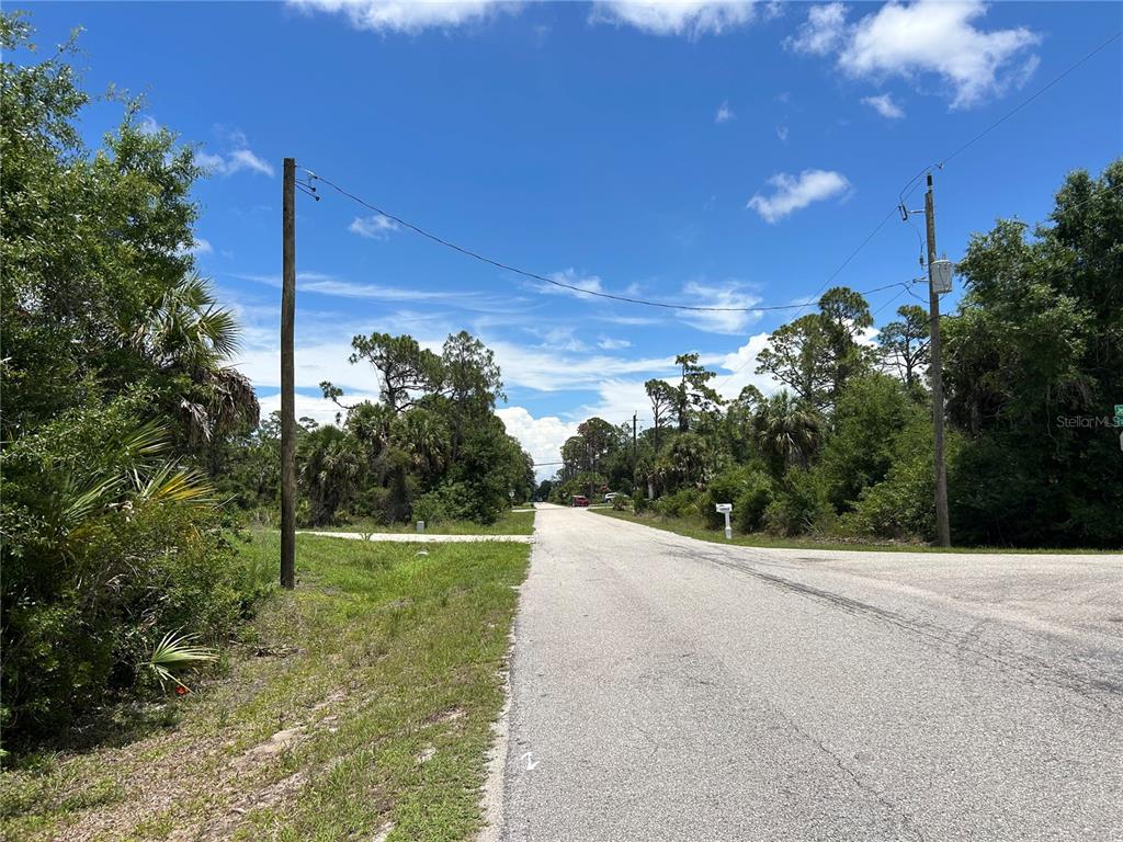 A paved road stretches into a wooded area under a bright blue sky — 17504 POSTON AVENUE, PORT CHARLOTTE, FL